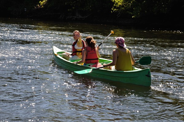 Two people paddling a green canoe on a sunlit river surrounded by nature, LA ROQUE GAGEAC FRANCE, Touristes en canoe sur le Dordogne. editorial