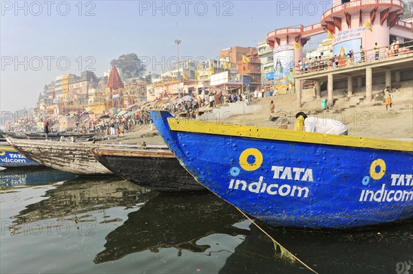 Boats on the banks of a busy river with colourful buildings in the background, Varanasi, Uttar Pradesh, India, Asia