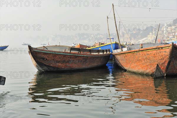 Stagnant boats on calm water with reflections and misty riverbank, Varanasi, Uttar Pradesh, India, Asia