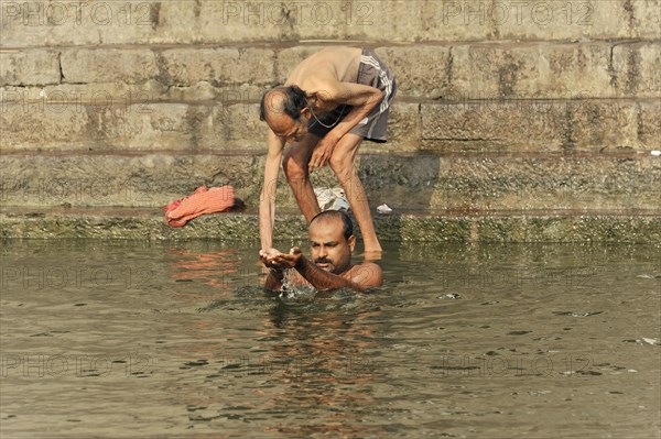 An elderly man helps another man to bathe himself in the river during a traditional ritual, Varanasi, Uttar Pradesh, India, Asia