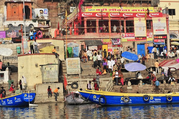 Colourful boats and people on the banks of a river with multi-storey buildings, Varanasi, Uttar Pradesh, India, Asia