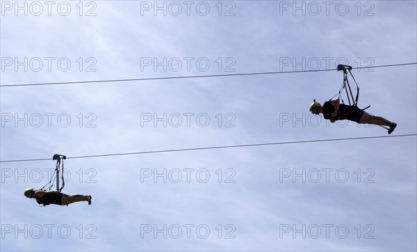 Two men use a zipline to fly over a 1, 000 metre stretch of the Rappbode Reservoir. The zipline, also known as a cable car or flying fox, is a cable connection between two points at different heights, Oberharz, 11 June 2017