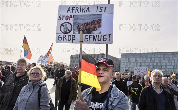 A participant in the Merkel muss weg demonstration wears an AFD cap and holds a sign reading Afrika ist gross genug (Africa is big enough) . Demonstration by right-wing populist and far-right participants, including supporters of the NPD, Pegida, Reichsbuerger, hooligans, Landsmannschaften and Identitarians, Berlin, 4 March 2017