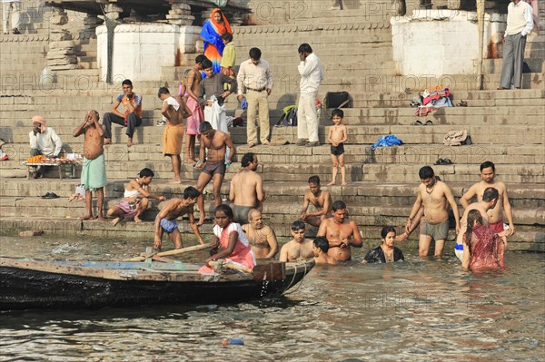 A boat passes a group of people bathing in the water at the river steps, Varanasi, Uttar Pradesh, India, Asia