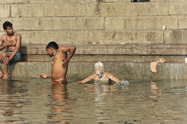 A man washing himself while swimming in the river next to the steps of the Ghats, Varanasi, Uttar Pradesh, India, Asia