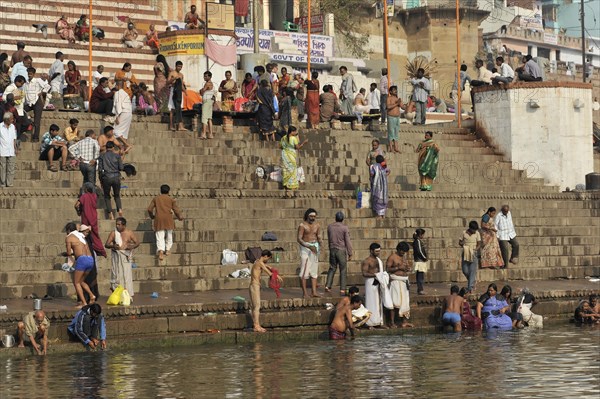 People washing clothes and bathing on the stone steps on the river bank with clear sky, Varanasi, Uttar Pradesh, India, Asia