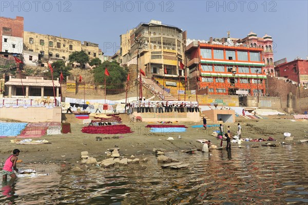 Vibrant riverside community with people tending to laundry in front of historic architecture, Varanasi, Uttar Pradesh, India, Asia