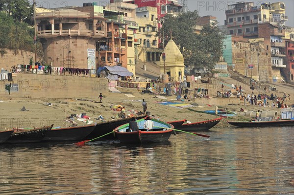 Boats at the edge of a river with people walking along the bank, Varanasi, Uttar Pradesh, India, Asia