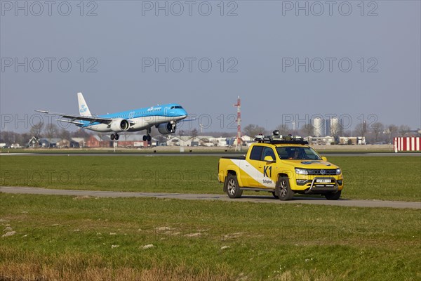 Bird Control Vehicle K1 patrols and KLM Cityhopper Embraer E195-E2 with registration PH-NXI lands on the Polderbaan, Amsterdam Schiphol Airport in Vijfhuizen, municipality of Haarlemmermeer, Noord-Holland, Netherlands