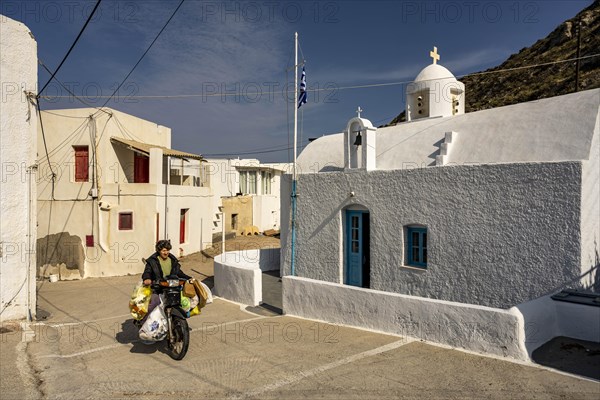 Woman riding a heavily loaded moped in front of Agios Dimitrios Church, Klima, Milos, Cyclades, Greece, Europe
