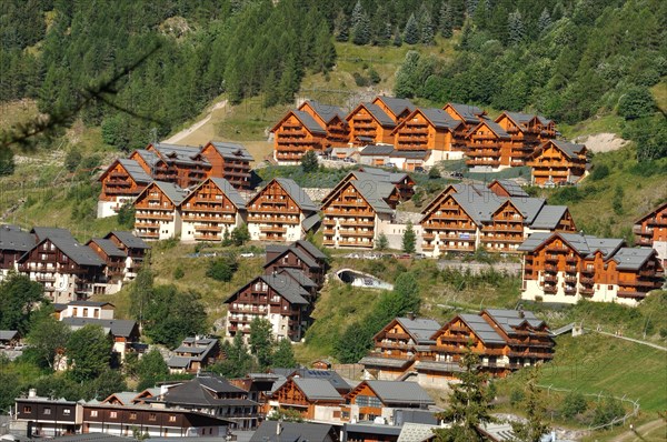 Alpine village with traditional chalets nestled among green trees on a hillside, Valloire