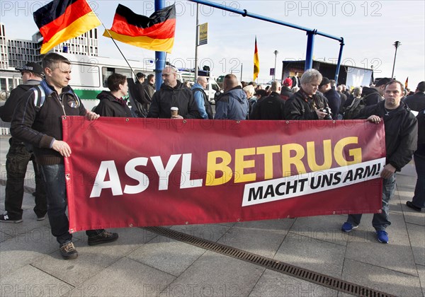 Participants in the Merkel muss weg demonstration hold a sign reading Asylum fraud makes us poor. Demonstration by right-wing populist and right-wing extremist participants, including supporters of the NPD, Pegida, Reichsbuerger, hooligans, Landsmannschaften and Identitarians, Berlin, 4 March 2017