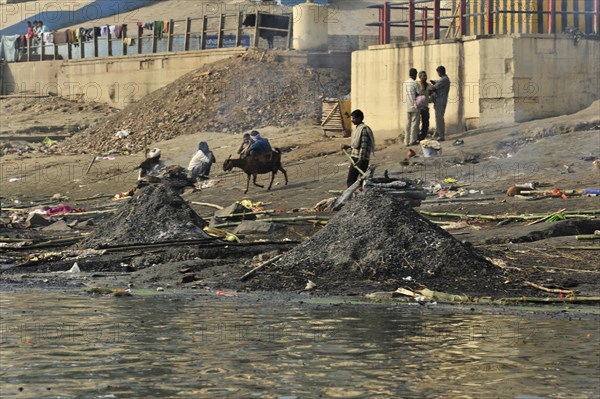 Busy riverbank full of people and animals, smoke and pollution emphasise the daily drama, Varanasi, Uttar Pradesh, India, Asia