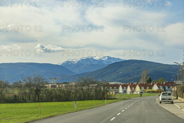 Road leads through a village with a view of the Schneeberg and a cloudy sky, Neunkirchen, Lower Austria, Austria, Europe