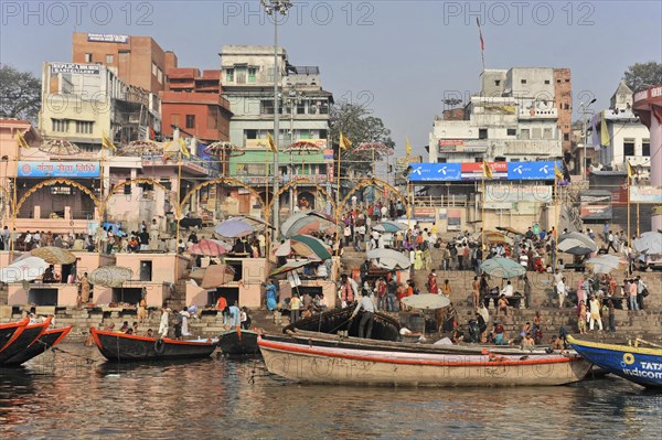 Densely populated shore with people, boats and umbrellas next to water body, Varanasi, Uttar Pradesh, India, Asia