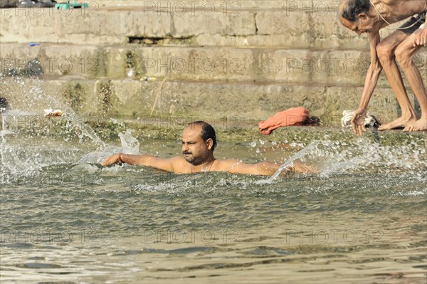 Two men bathing in the river, with water splashes around the swimmer, Varanasi, Uttar Pradesh, India, Asia