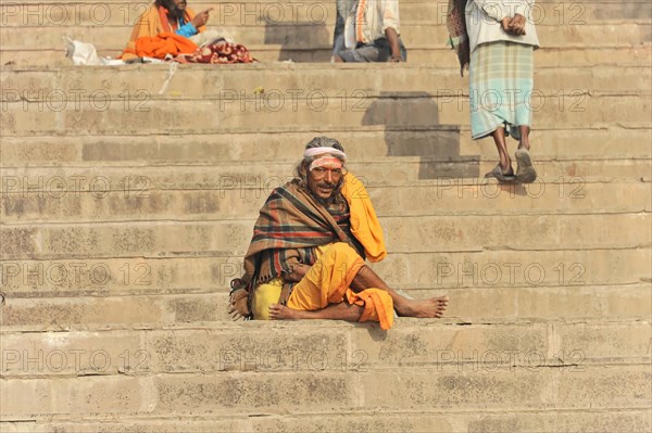 Relaxed looking man sitting on steps in front of an urban backdrop, Varanasi, Uttar Pradesh, India, Asia