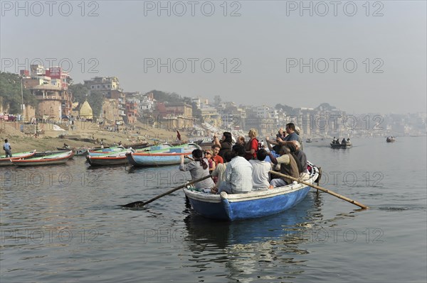 Boat with passengers on a river, rowers at the stern, city view in the light morning mist in the background, Varanasi, Uttar Pradesh, India, Asia