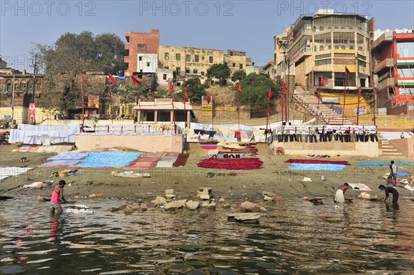 Children playing on the banks of a river while others do laundry, against an urban background, Varanasi, Uttar Pradesh, India, Asia