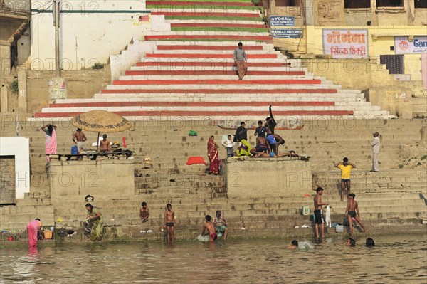 People on river steps, some bathing in the water, with a parasol in the background, Varanasi, Uttar Pradesh, India, Asia