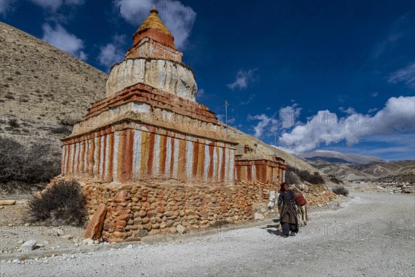 Woman with her horse, colourfully painted Buddhist stupa in front of mountain landscape, erosion landscape and houses of Garphu behind, Garphu, Kingdom of Mustang, Nepal, Asia