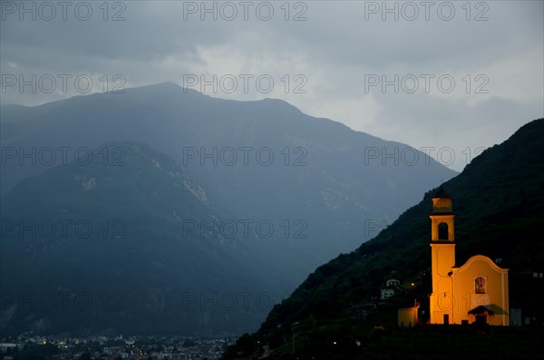 Illuminated Church on the Mountains at Night withStorm Clouds in Bellinzona, Ticino, Switzerland, Europe