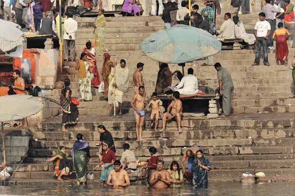People bathing in the river on a sunny day with umbrellas on steps, Varanasi, Uttar Pradesh, India, Asia