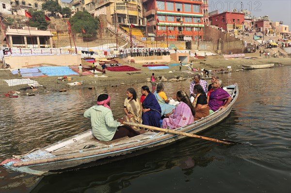 People on a boat on a river in front of a staircase with colourful buildings, Varanasi, Uttar Pradesh, India, Asia