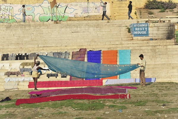 People hanging colourful laundry on a sunny riverside staircase, Varanasi, Uttar Pradesh, India, Asia