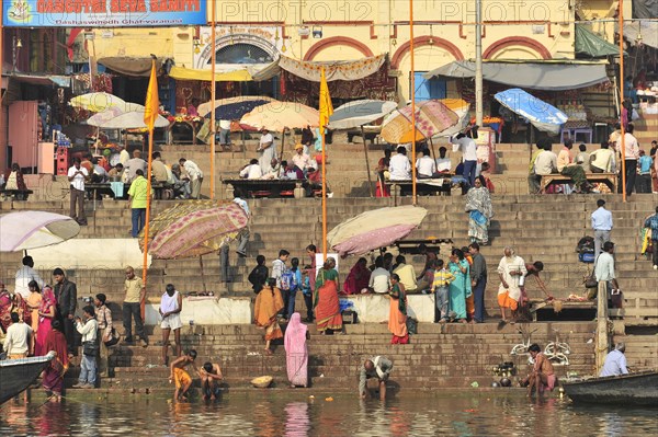Lively social scene with many people and parasols at the ghats of a river, Varanasi, Uttar Pradesh, India, Asia