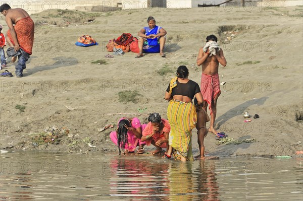 A family performs a traditional ritual at the water's edge of a beach, Varanasi, Uttar Pradesh, India, Asia