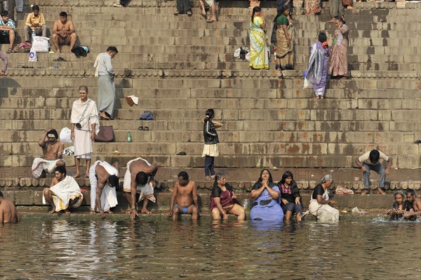People bathing and washing on the steps of a river, some in traditional dress, Varanasi, Uttar Pradesh, India, Asia