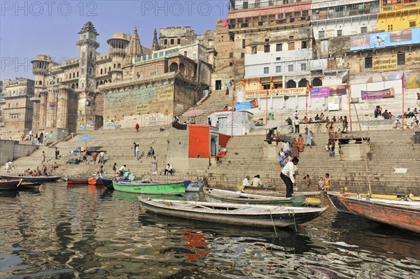 Busy riverbank with boats and people against the backdrop of urban architecture, Varanasi, Uttar Pradesh, India, Asia