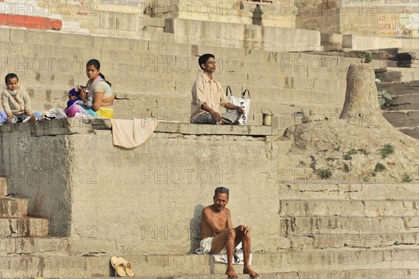 Several people sit relaxed on the ghats of a river and interact with each other, Varanasi, Uttar Pradesh, India, Asia