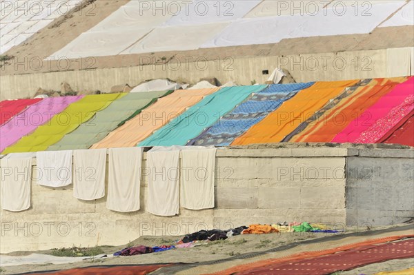 A row of colourful textiles drying in the sun on a riverbank, Varanasi, Uttar Pradesh, India, Asia