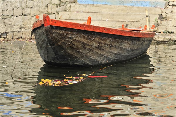 A single boat floats with a flower offering on the calm waters of a river in India, Varanasi, Uttar Pradesh, India, Asia