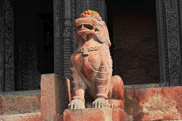 Stone lion statue with flower necklace in front of a carved temple background, Varanasi, Uttar Pradesh, India, Asia