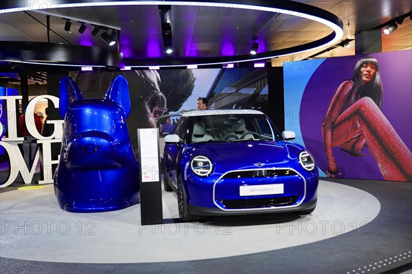 A blue Mini Cooper is presented at a car show next to a large model head, BMW WELT, Munich, Germany, Europe