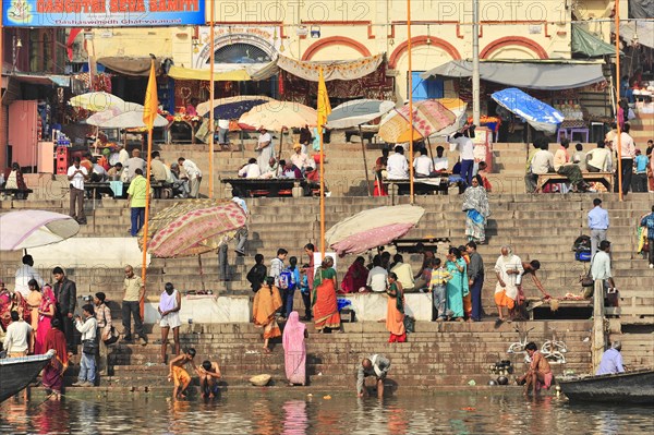 People at the ghats of a river under umbrellas with urban background, Varanasi, Uttar Pradesh, India, Asia