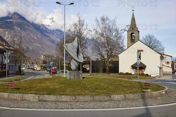 Bell tower with church Clocher de la chapelle St. Michel, art in the roundabout by Antoine Poncet and mountains with clouds in the background in Martigny, district of Martigny, canton of Valais, Switzerland, Europe