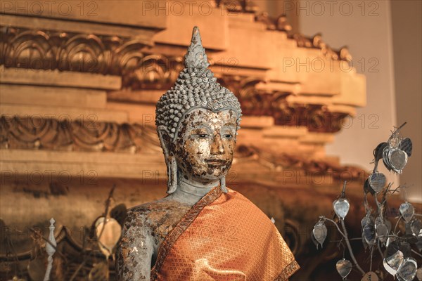 Gilded Buddha statue with worn texture wrapped in orange fabric. Ayutthaya, Thailand, Asia