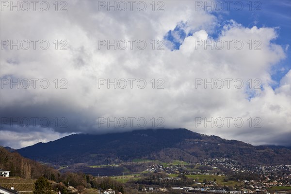 Mighty white spring clouds move under a blue sky over a wooded hill near Jongny, Jongny, Riviera-Pays-d'Enhaut district, Vaud, Switzerland, Europe