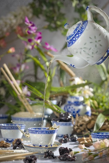 Tea splashes out of the bowl of an Asian tea set as it is poured, flying pot, flowers in the background