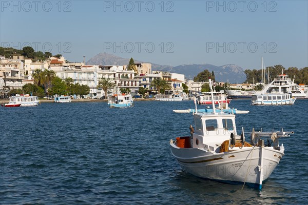 Fishing boat on clear blue water in front of a coastline with architecture, Galatas, Argolis, Peloponnese, Greece, Europe