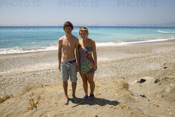 Model released smiling brother and sister twins stand on sandy beach together, Rhodes, Greece, Europe