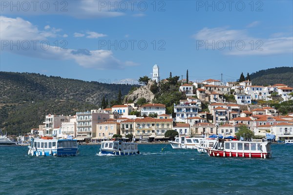 View of a lively harbour with colourful houses in front of a hill under a blue sky with clouds, water taxi, view from Galatas, Argolis, to Poros, Poros Island, Saronic Islands, Peloponnese, Greece, Europe