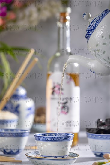 Pouring tea, Asian tea set with blue patterns, a bottle of China plum wine in the background, dried fruit