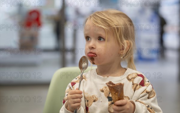 Interior shot, girl, 2-3 years, blonde, eating chocolate ice cream, ice cream, waffle, spoon, mouth smeared, logo, pharmacy, Stuttgart, Baden-Wuerttemberg, Germany, Europe