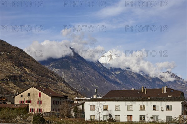 Residential buildings and pointed, high mountains with clouds in Martigny, district of Martigny, canton of Valais, Switzerland, Europe