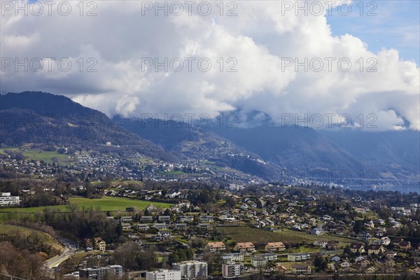 View of the outskirts of Vevey and mighty white spring clouds moving over mountains near Jongny, Jongny, Riviera-Pays-d'Enhaut district, Vaud, Switzerland, Europe